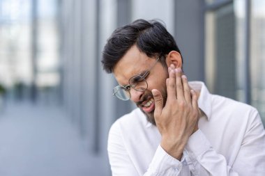 Kulağını işyerinde ağrı ve rahatsızlık içinde tutan genç bir adam kulak ağrısı, enfeksiyon veya kulak çınlaması, stres ve tıbbi bakım ve yardım ihtiyacı belirtileri gösteriyor.