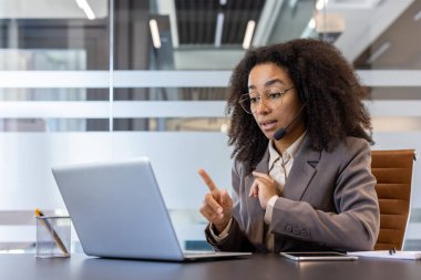 Kulaklık takmış genç bir Afro-Amerikan kadın dizüstü bilgisayarda oturuyor ve online danışmanlık yapıyor..