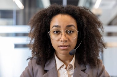 Ofiste dikilip kameraya bakan ciddi ve konsantre olmuş Afro-Amerikan bir kadının yakın plan portresi..