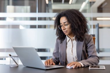 Ciddi Afrikalı genç iş kadını bir dizüstü bilgisayarın ofisinde çalışıyor..