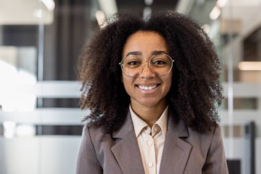 Gülümseyen ve başarılı bir Afrikalı Amerikalı iş kadınının yakın plan portresi ofiste duruyor ve kendine güvenerek kameraya bakıyor..