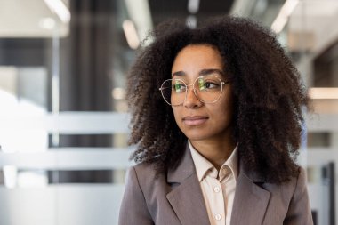 Ofiste olup gözlerini kaçıran takım elbiseli, ciddi ve kendine güvenen Afro-Amerikan bir kadının yakın plan fotoğrafı..