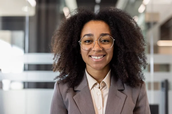Gülümseyen ve başarılı bir Afrikalı Amerikalı iş kadınının yakın plan portresi ofiste duruyor ve kendine güvenerek kameraya bakıyor..