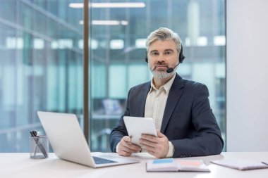 Çağrı merkezinde çalışan, kulaklık takan, tablet tutan, müşteri desteği sağlayan ya da modern bir ofis masasından tele pazarlama hizmeti veren ciddi bir iş adamı.
