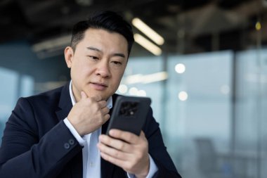 Genç ve ciddi bir Asyalı adamın telefonuna dikkatlice bakarken yakın plan fotoğrafı..