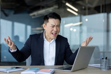 Angry and frustrated young businessman shouting into laptop while talking on online meeting.
