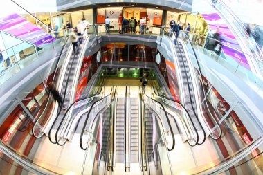 Yürüyen merdivende hareket halindeki bir alışveriş merkezinde alışveriş yapanlar