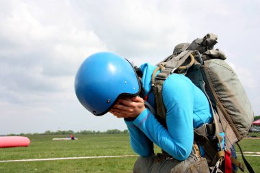 Mavi kazaklı ve kasklı kız, sırtındaki paraşüt atlayışından korkarak elleriyle yüzünü örttü.