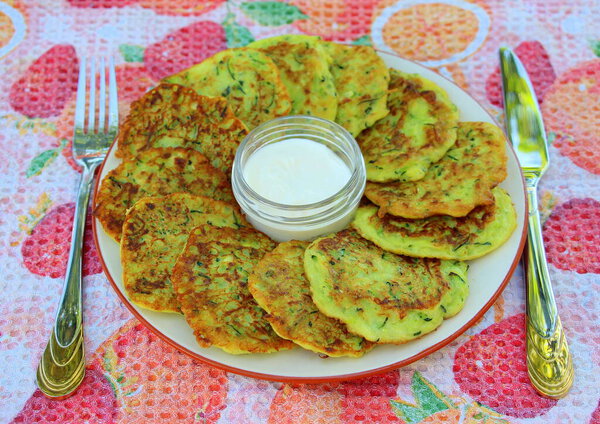 Zucchini pancakes fried in olive oil with sour cream in the summer at the dacha. Delicious, vegetable and healthy breakfast.