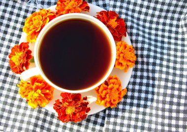 Beyaz bardakta sade kahve ya da çay. Bir çay tabağında taze doğal Çernobil kadife çiçekleri. Siyah beyaz ekose kumaş