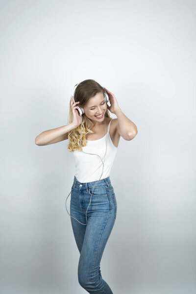 blond woman holding her headphones with both hands listening to music smiling white isolated background