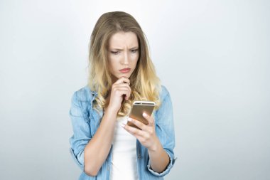 sarışın genç kadın elinde izole beyaz arka plan akıllı telefon şaşırmış görünüyor