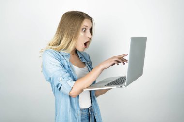 genç sarışın kadın onu laptop izole beyaz arka plan parmağıyla işaret şaşırmış görünüyor