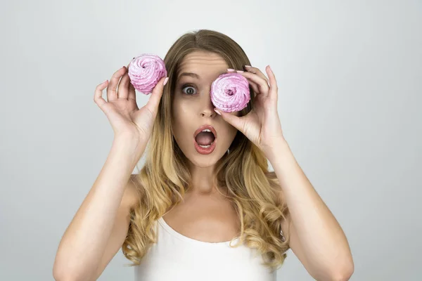 Legrační atraktivní dívka s jedním dortem u oka, které drží další koláč v její ruce vypadá překvapeně izolované bílé pozadí — Stock fotografie