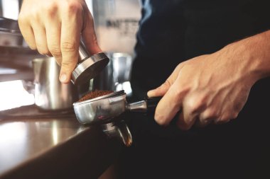 Kahveyi bir elinde tutan barista müşteriye espresso yapmak için tutacakta öğütülmüş kahveye basacak.