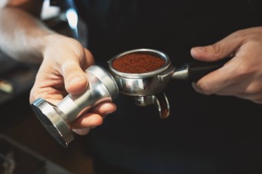 barista adam bir elinde öğütülmüş kahve ile kahve tutucu tutan ve başka bir kafeyakın americano hazırlanıyor bir kurcalamak