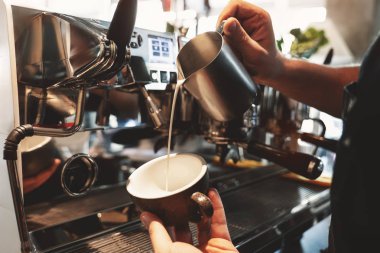 barista adam kafede profesyonel kahve makinesi yakınında duran kahve ile fincan köpüklü sürahi gelen çırpılmış süt dökme