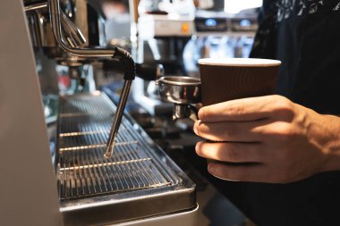 barista adam bir elinde kağıt fincan sıcak kahve içeceği tutan ve kahve tutucu başka bir kafede profesyonel kahve makinesi yakınında yakın ayakta