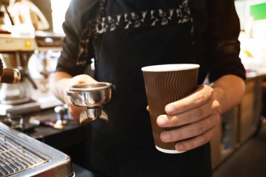 barista adam bir elinde kağıt bardak sıcak kahve içeceği tutan ve başka bir kafede profesyonel kahve makinesi yakın duran kahve tutucu