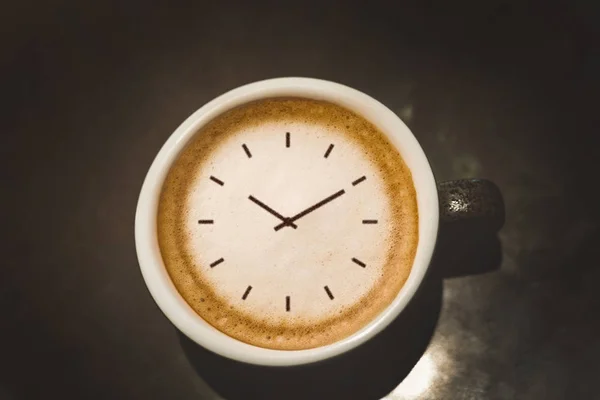 cappuccino cup with clock face standing on black table close up