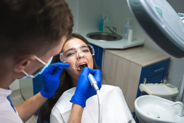 Dentista en máscara que llena el conducto radicular de los pacientes mientras ella está acostada en la silla dental con gafas de seguridad debajo de la lámpara médica en la clínica — Foto de Stock