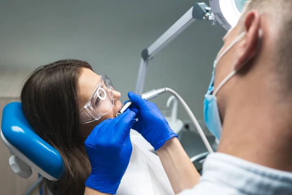 Dentista en máscara médica que llena el conducto radicular de los pacientes mientras ella está acostada en la silla dental con gafas de seguridad — Foto de Stock
