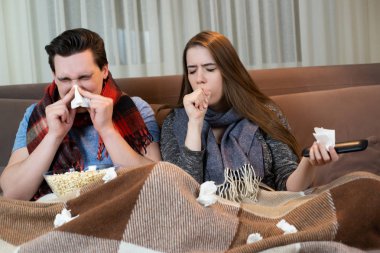 genç çift kanepede film izlerken yakışıklı adam burnunu üfleme ve çekici kadın hem hasta görünümlü eşarp giyen öksürük