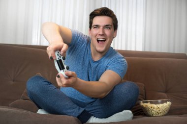 genç yakışıklı adam eğlenceli kanepede otururken görev dahil görünümlü iki eliyle joystick tutarak