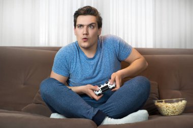 Genç yakışıklı adam oynamak video oyunu rahat Sofa tutarak joystick üzerinde oturan çok misyon üzerinde konsantre görünüyor