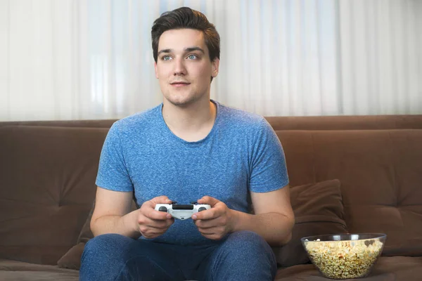 Joven guapo hombre jugando video juego sentado en cómodo sofá —  Fotos de Stock