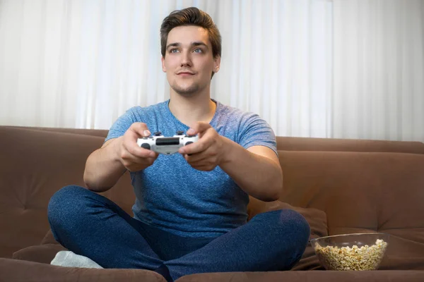 Joven guapo hombre jugando video juego sentado en cómodo sofá celebración de joystick —  Fotos de Stock