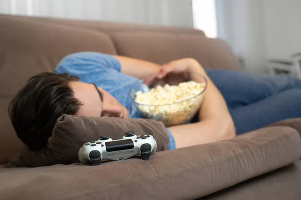 Joven guapo hombre se duermen después de jugar fascinante videojuego todavía sosteniendo palomitas de maíz en sus manos —  Fotos de Stock