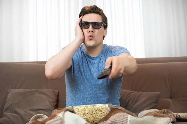 Joven sorprendido hombre usando gafas de sol viendo película comer palomitas de maíz clic control remoto se ve asombrado —  Fotos de Stock