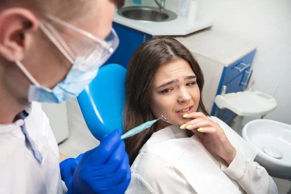 Beautiful scared frightened patient woman having examination at dental office by handsome dentist in mask and blue gloves — Stock Photo, Image