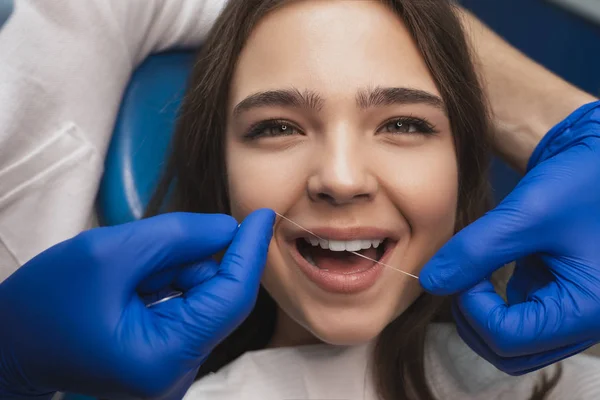 Dentista en guantes médicos azules la limpieza de los dientes de las mujeres pacientes utilizando hilo dental en la clínica — Foto de Stock