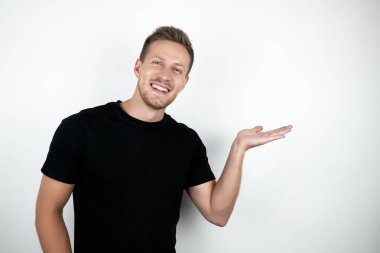 beyaz arka plan üzerinde izole ayakta iken siyah t-shirt gülümseyen ve kopya alanı tutan giyen yakışıklı genç adam
