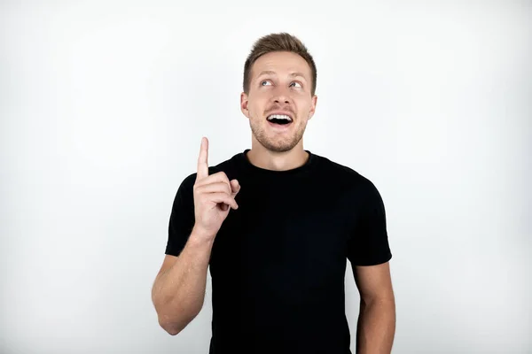 Bonito jovem surpreso homem no preto t-shirt apontando com o dedo para cima isolado branco fundo — Fotografia de Stock