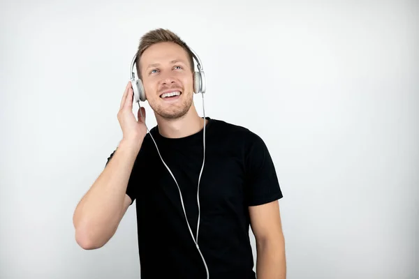 Joven guapo con camiseta negra escuchando música en auriculares aislados fondo blanco —  Fotos de Stock