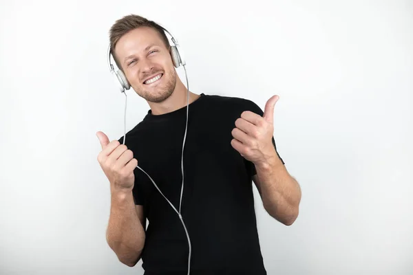 Joven guapo con camiseta negra escuchando música en auriculares que muestran un cartel aceptable con ambas manos sobre un fondo blanco aislado —  Fotos de Stock