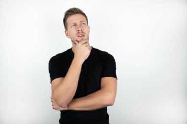 bir eliyle yüzüne dokunarak siyah t-shirt giyen yakışıklı genç adam dalgın izole beyaz arka plan görünüyor