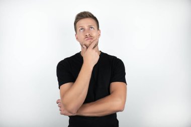 bir eliyle yüzüne dokunan siyah t-shirt giyen yakışıklı genç adam düşünceli izole beyaz arka plan görünüyor