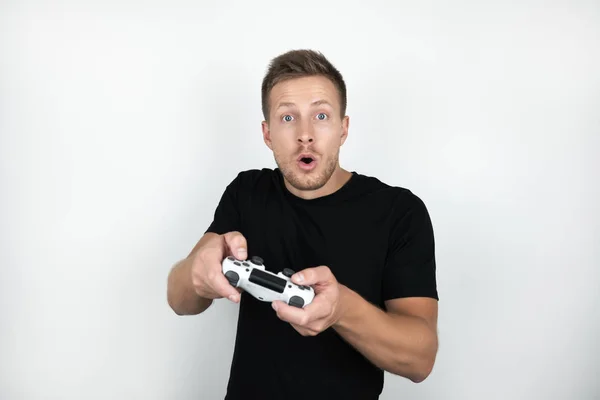 Joven guapo vistiendo camiseta negra sosteniendo joystick en sus manos juega video juego aislado fondo blanco —  Fotos de Stock