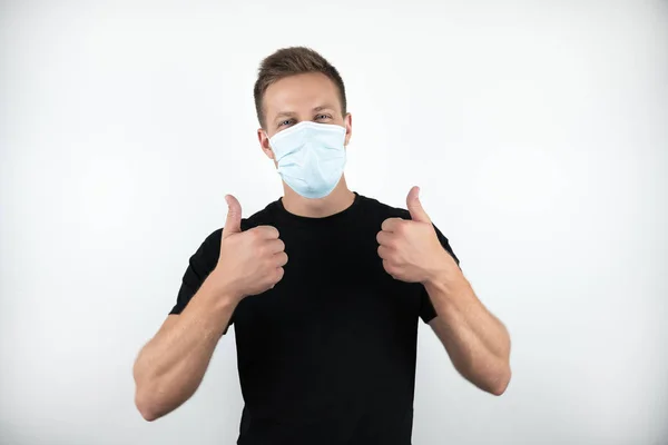 Красивый молодой человек в черной футболке в медицинской маске показывает знак ОК с обеими руками на изолированном белом фоне — стоковое фото