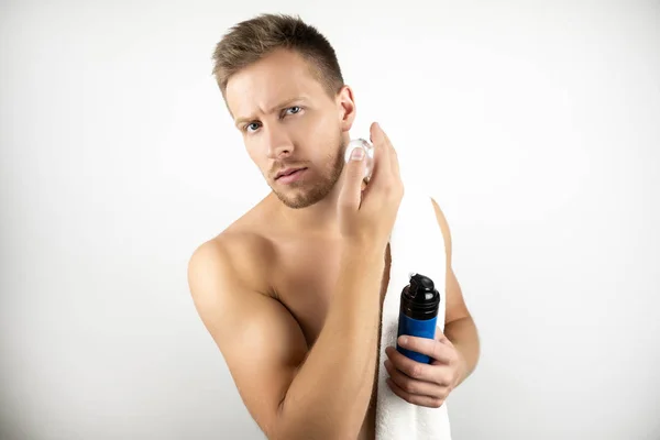 Изображение красивого мужчины с белым полотенцем на плече, нанося пену для бритья на лицо во время утренней рутины на белом фоне — стоковое фото