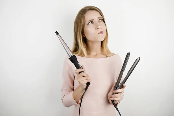 Joven hermosa mujer vistiendo vestido rosa de moda sosteniendo rizador y streightener pelo sobre fondo blanco aislado — Foto de Stock