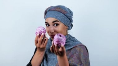 izole beyaz arka plan üzerinde eğlenceli bir ruh hali içinde lezzetli cupcakes tutarak gülümseyen genç güzel arap kadın