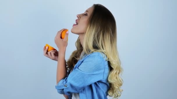 Joven hermosa rubia lamiendo una mitad de naranja fresca sobre fondo blanco aislado — Vídeo de stock