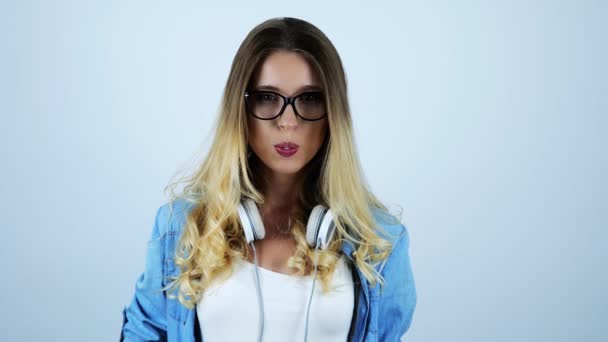 Izole beyaz arka plan üzerinde boynunda kulaklık ile köpüklü sakız şişirme gözlük genç güzel sarışın kadın — Stok video