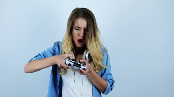 Joven hermosa mujer rubia sexy con auriculares en su cuello jugando videojuego mirando emocionado sobre fondo blanco aislado — Vídeo de stock