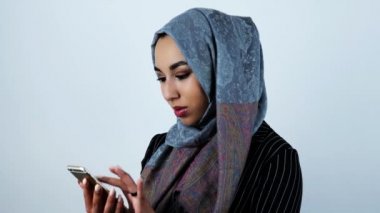 izole beyaz arka plan üzerinde akıllı telefon kaydırma sırasında genç güzel arap kadın gülümsüyor